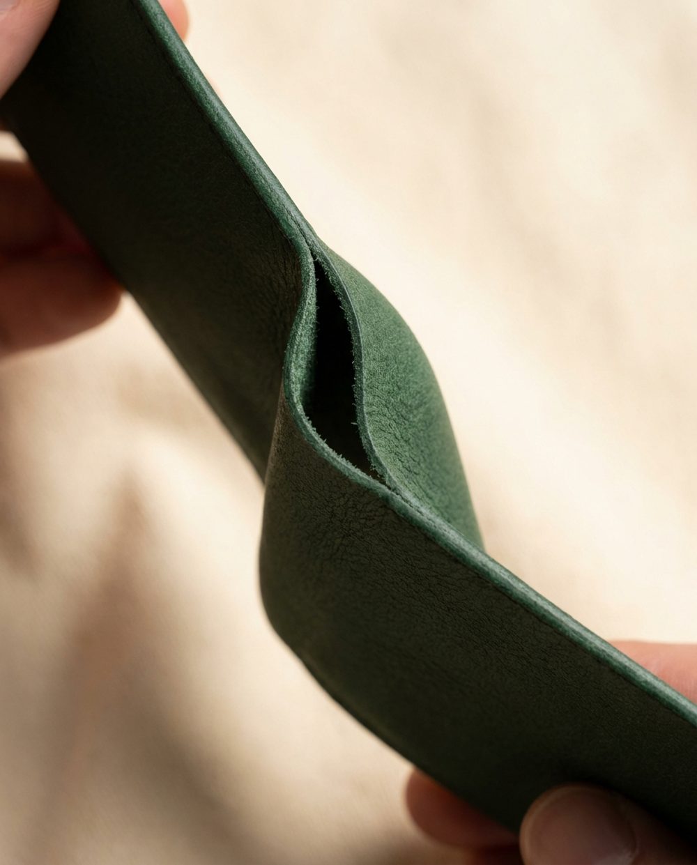 A thin sheet of forest green calf leather folded by hand into a tight crease, showing the flesh side and no cracking of the finish
